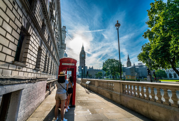 Big ben on the background and red telephone booth with two tourists in London at sunrise