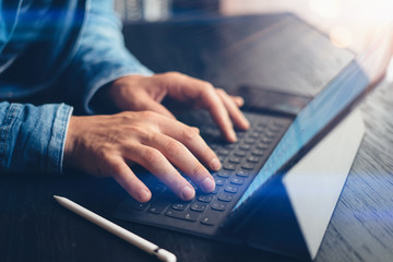 Closeup view of male hands typing on electronic tablet keyboard-dock station. Man working at office.Horizontal,flares effect.