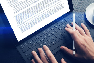 Closeup view of male hands typing on electronic tablet keyboard-dock station. Man working at office.Horizontal.