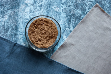 Superfood raw unroasted kerob in glass bowl on blue background. Bright colorful flat lay of healthy product.
