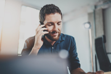 Bearded smiling businessman working at sunny office.Man using contemporary smartphone.Horizontal.Blurred background.