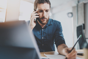 Bearded serious businessman working at sunny office.Man using contemporary smartphone for making call.Horizontal.Blurred background.