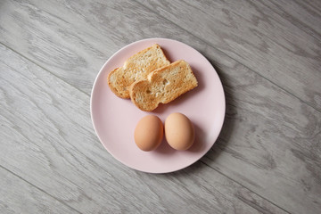 Healthy breakfast. Boiled chicken eggs and toast on a pink plate. Gray wooden background.