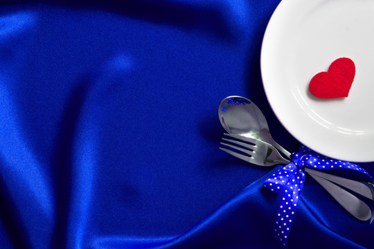 red heart shape with White empty plate with fork and spoon on blue silk fabric for love dinner concept