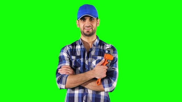 Confident Caucasian plumber crossed arms while smiling and holding an adjustable wrench in front of green screen background