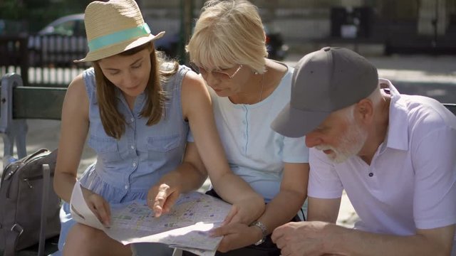 Happy family enjoying vacation together. Seniors and their young daughter studying city map looking for showplaces. Lost in city looking for directions