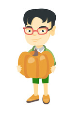 Cheerful asian boy standing with a big orange pumpkin in hands