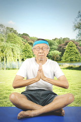 Naklejka na ściany i meble Elderly man doing yoga in the park
