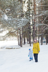 mother with son goes by the hand in the winter pine forest