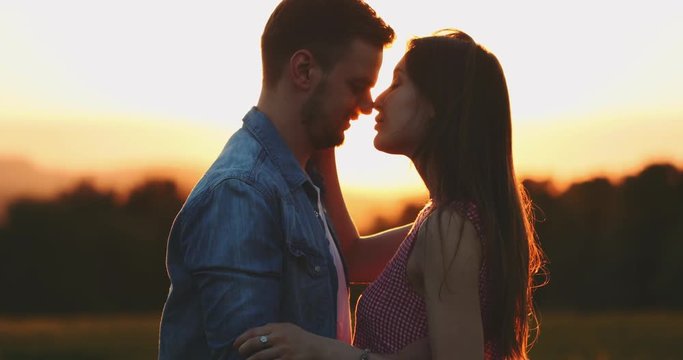 Young Couple Kissing at Sunset. SLOW MOTION 4K, Close Up. Romantic man and woman in love share a kiss. Love and affection. Cinematic backlit shot, Lens Flare.