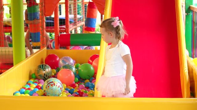 Sweet modest little girl playing in game center. Portrait of little girls playing on the Playground with a ball pit and a slide.