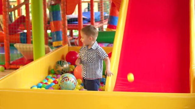 Portrait of little boy in shorts and shirt playing on the Playground with a ball pit and a slide. Little boy playing on a colorful Playground.