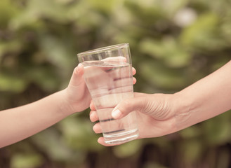 Closeup vintage woman hand giving glass of fresh water to child in the park.  Drink and health care concept.