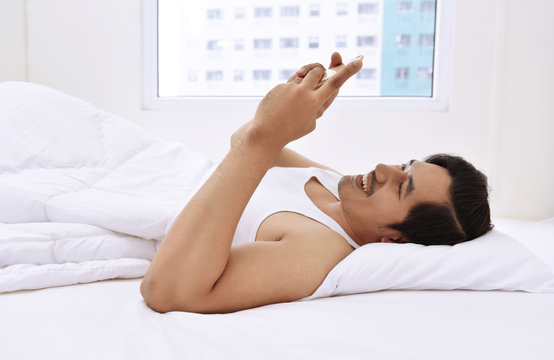 Happy asian man lying down and using mobile phone