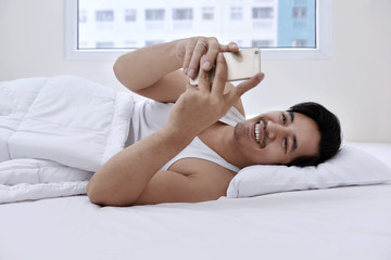 Handsome asian man lying in bed with smartphone