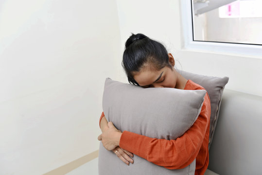 Sad asian woman hugging a pillow and sitting on sofa