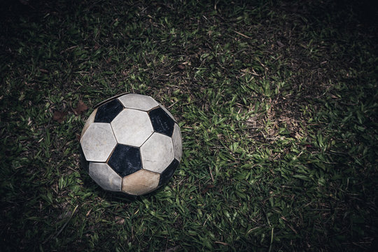 Old soccer ball or football lay on green grass for kick. Low key picture style.