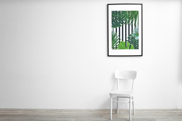 Framed picture of tropical leaves and wooden chair on white wall background