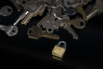 Gold padlock and metal keys on shiny, black background