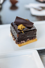 Square chocolate cake with chocolate ganache topping with minced eatable gold paper and chocolate plate at the cafe in Dubai. 