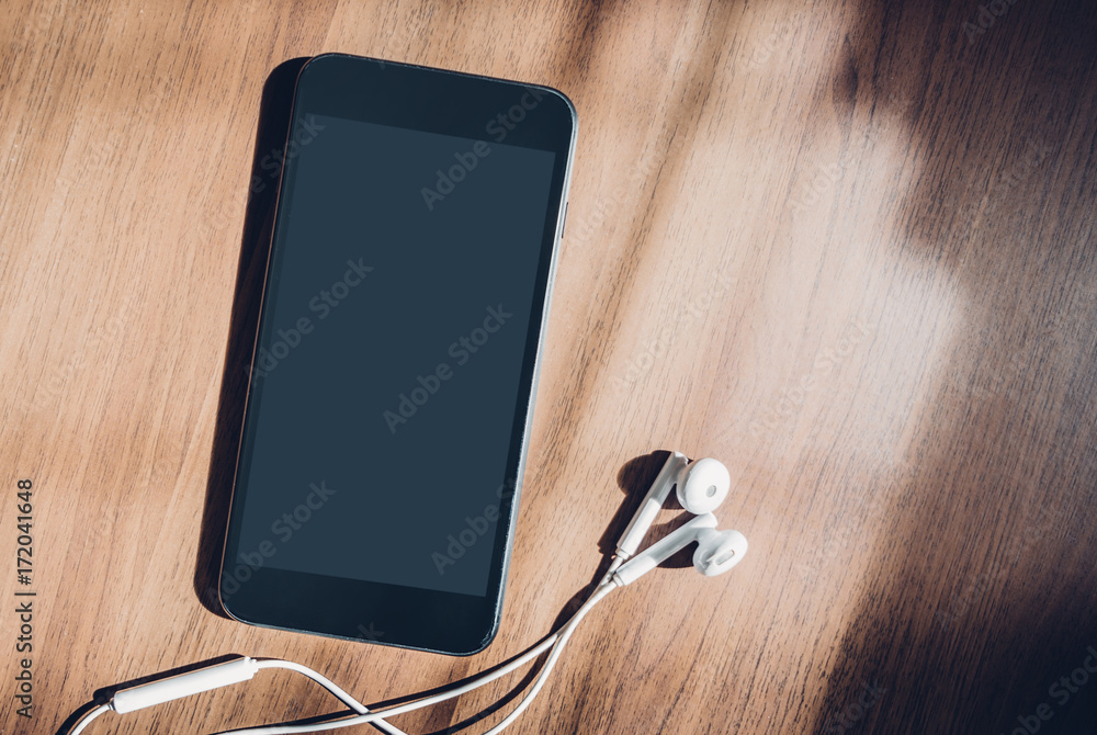 Poster blank mobile screen with earphones lay on brown table near window sunlight at afternoon,music lover 