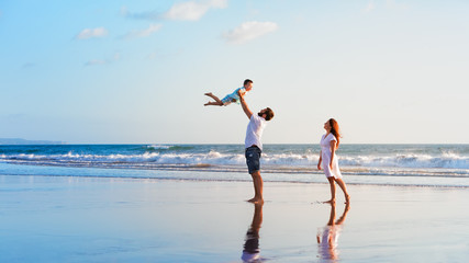 Happy family holidays. Joyful father, mother, baby son walk with fun along edge of sunset sea surf...