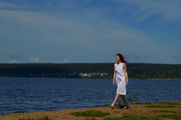 Beautiful woman in white dress walking near the river bank