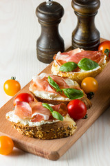Italian tomato, prosciutto, jamon, ham and cheese bruschetta. Tapas, antipasti with chopped vegetables, herbs and oil on grilled ciabatta and baguette bread.