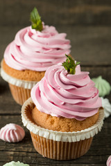 Closeup of cupcakes with vanilla, berries, pink and white cream, chocolate and sprinkles on wooden background. Selective focus. Sweet dessert tasty food concept muffin.