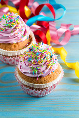 Closeup of cupcakes with vanilla, berries, pink and white cream, chocolate and sprinkles on wooden background. Selective focus. Sweet dessert tasty food concept muffin.