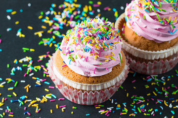 Closeup of cupcakes with vanilla, berries, pink and white cream, chocolate and sprinkles on wooden background. Selective focus. Sweet dessert tasty food concept muffin.