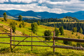 rural fields behind the wooden fence on hills in mountainous area. lovely countryside landscape in...