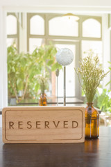 Wooden reserved table sign with empty steel label for table in restaurant with small flower vas.