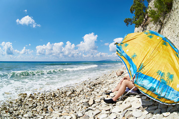 Man resting on rocky beach under umbrella