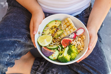 buddha bowl with tofu, broccoli and vegetables in the hands of a child