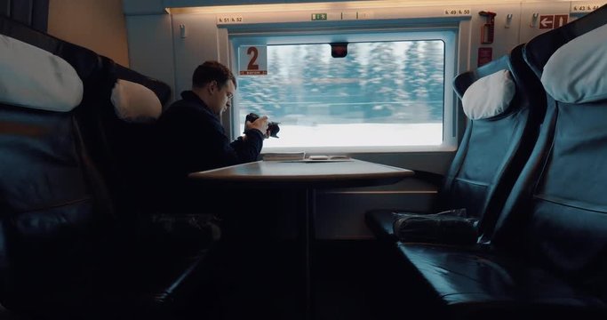 Man with camera taking video of passing snowy pinery landscape when traveling in first class carriage of express train