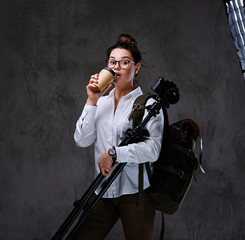 Fototapeta na wymiar Female holds digital photo camera and takeaway coffee over grey background.