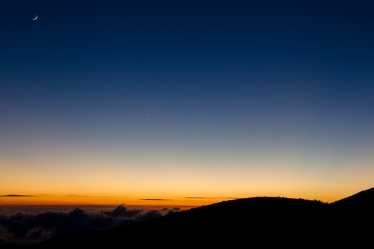 Mondsichel über dem vom Sonnenuntergang erleuchteten Horizont am Mauna Kea auf Big Island, Hawaii, USA.