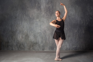 Fototapeta na wymiar beautiful young blonde ballet dancer in a black dress, white pantyhose and bouillant pointes dancing Russian ballet in a dark dance studio