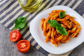 Penne with tomato sauce and basil on wooden background