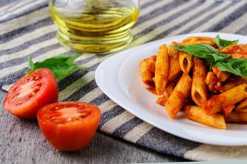 Penne with tomato sauce and basil on wooden background