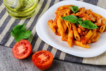 Penne with tomato sauce and basil on wooden background
