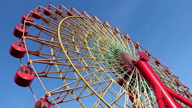 Ferris wheel with red cabins rotate against blue sky, Kobe, Japan.