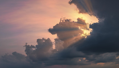 Sun rays shining through beautiful rain clouds at dusk. Dramatic cloudscape at sunset.