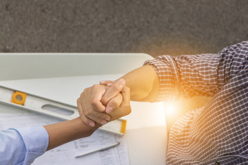 Obraz premium Top view of construction engineer team and business man shaking hands after meeting at construction site with blurred plan and tools background, success teamwork concept.