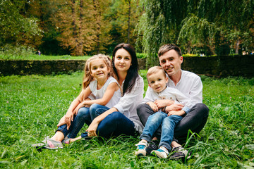 Naklejka na ściany i meble portrait of happy family mother, father, duaghter and son sit on the ground