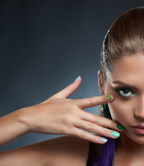 Obraz premium Crop of beautiful confident woman with perfect makeup posing in studio, looking at camera, touching face by hand. Brunette girl after beauty salon, with long violet earring showing shine manicure.
