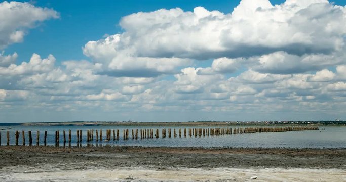 Time lapse of running clouds under the wooden posts of old jetty in abandoned salt farm near Kuyalnik estuary. 4K