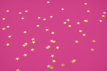 Golden star sprinkles on pink. Festive holiday background. Celebration concept. Top view, flat lay. Horizontal