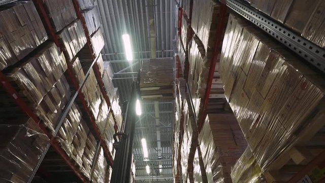 Forklift in the warehouse raises a boxes toward the top shelf. Warehouse materials. Shelves in the warehouse.
